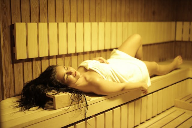 nainen makaa pyyhe päällä saunan lauteilla
