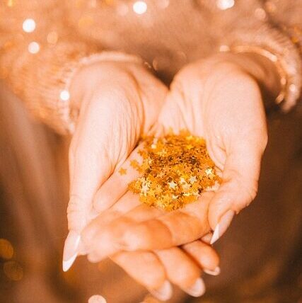 naisella on käsissään tähden muotoisia kultaisia glittereitä